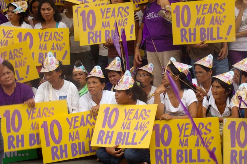 Photo of a large group of people, each holding large yellow signs with purple writing that says 