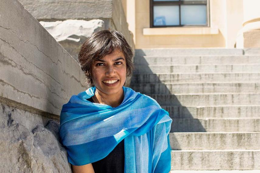 Headshot of a smiling person with a background of concrete stairs and columns.