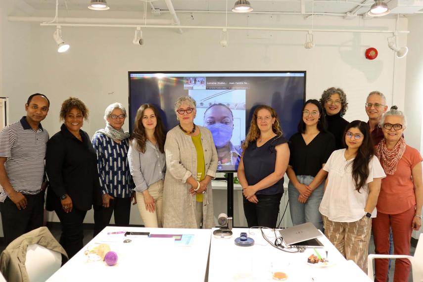 Group photo of 12 people. One person is on a large tv screen.