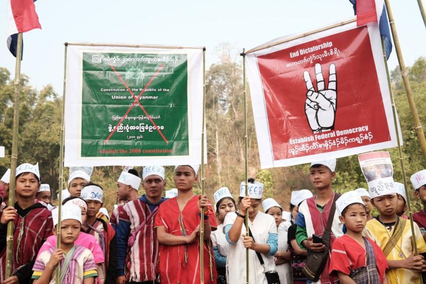 Group photo of about 25 children and youth. Each wears a cylindrical paper hat on their head, some with the word
