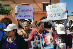 Women gather together outside holding signs that read 'Welcome mothers' and signs with photos of missing children