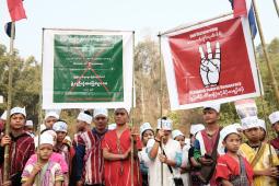 Group photo of about 25 children and youth. Each wears a cylindrical paper hat on their head, some with the word "Freedom" written on them. A few of the youth are holding up two large protest signs.