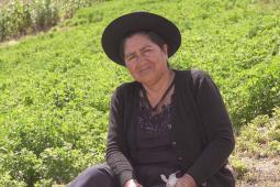 Photo of a woman looking solemnly into the camera. She's sitting on a grassy slope.