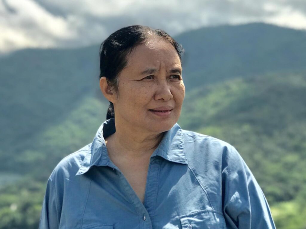 International aid cuts directly impact Dr. Cynthia. Here, she looks into the distance. There are mountains around her in the background.