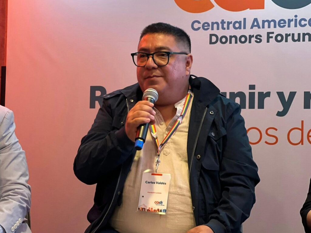USAID International aid cuts impact Carlos's work. Here, he holds a microphone as he speaks on a panel.