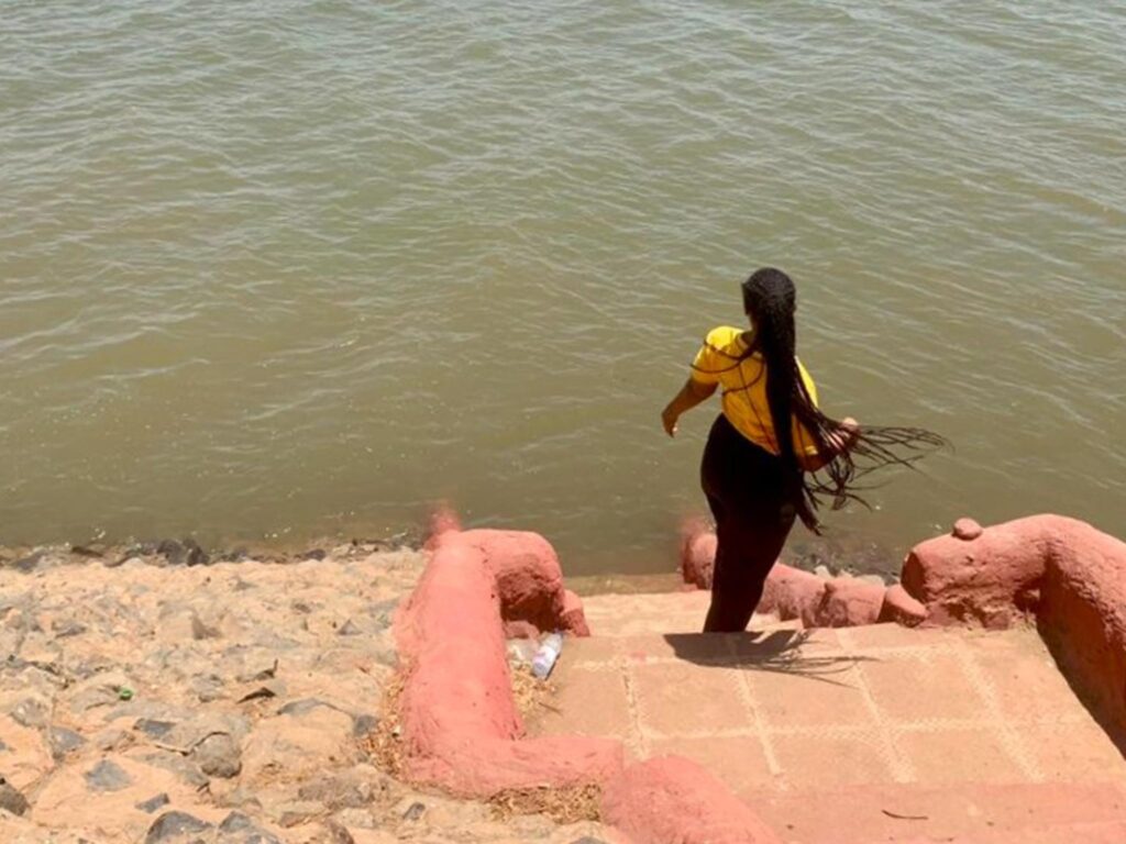 Sudan war: Donate now to support the woman in this photo, Reham. Here she lhas her back to the camera and there is a river in front of her.