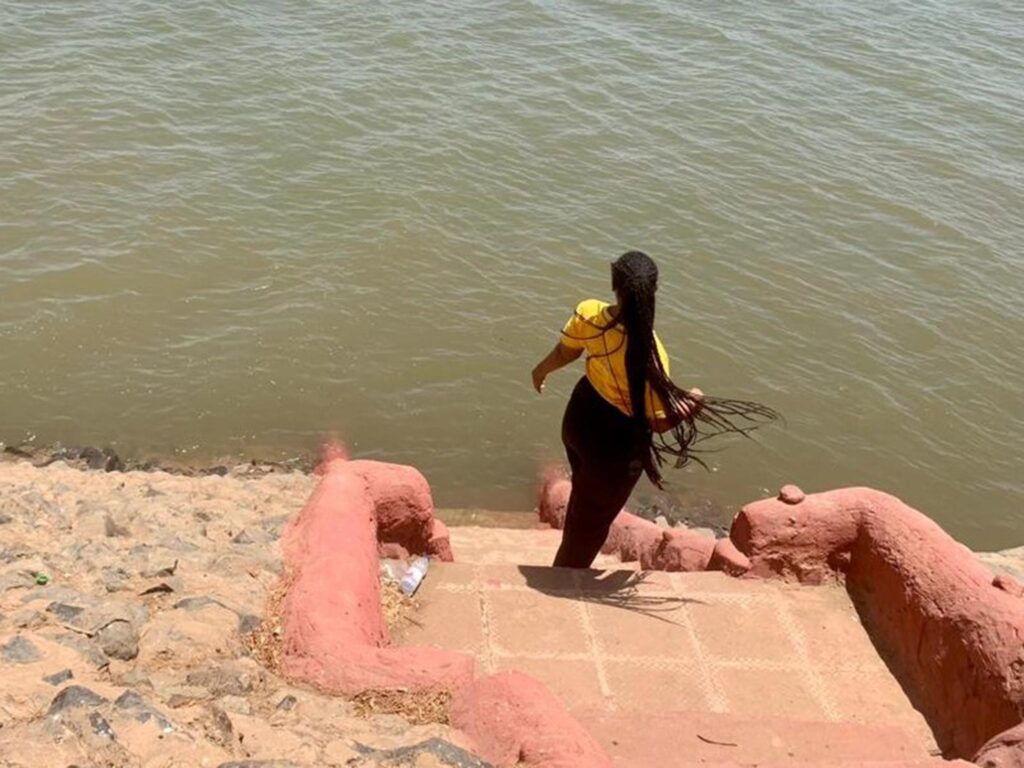 U.S.-based international aid cuts impact Reham's work with Sudanese LGBTQI+ community. Here, she looks toward a river with her back to the camera.