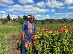 Mariamé Ouattara stands among vibrant flowers in a rural garden landscape beneath blue skies, celebrating agriculture, biodiversity and community.